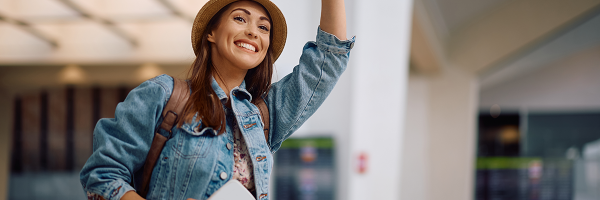 Should I cancel my trip? Smiling woman waving outside of the airport.